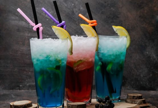 Close-up alcohol cocktails glasses of blue lagoon cocktail decorated with lemon and glass of cocktail with whiskey on a wooden stand